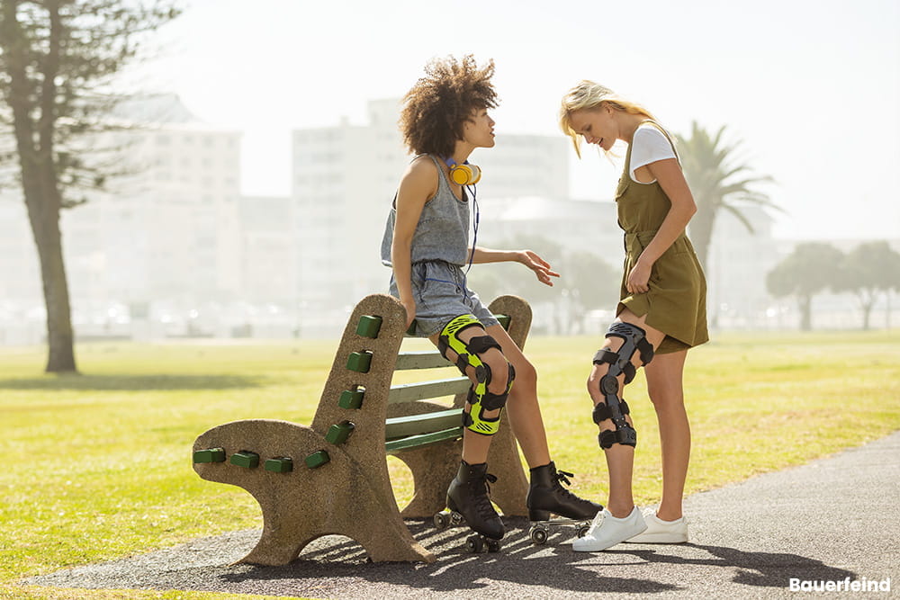 Zwei Frauen stehen an einer Bank und unterhalten sich, beide tragen eine Beinorthese.